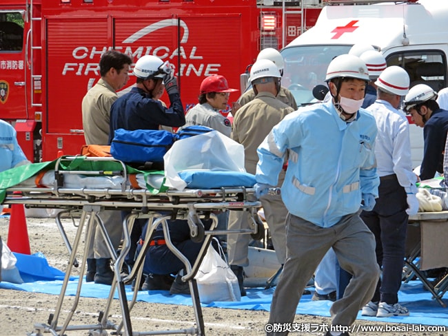 岸和田市消防本部の感染防止衣を着用した救急救命士が救急資器材をストレッチャーに乗せて駆けつける様子。